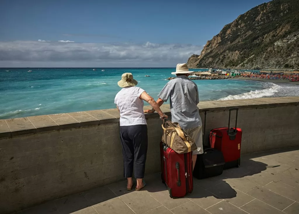 An elderly couple with their travel luggage looking out over the sea