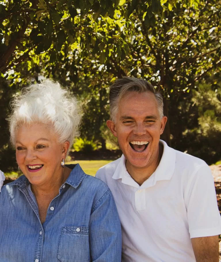 An adult son laughing together with his elderly mother outdoors
