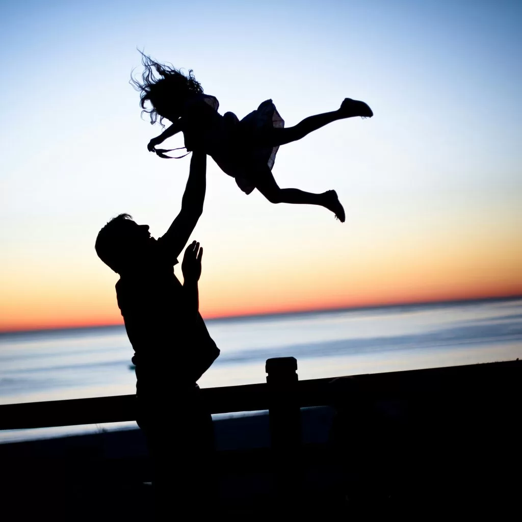A father lifting his child into the air at sunset by the sea